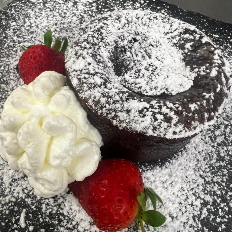 Schokokuchen Schokoladenkuchen mit Puderzucker, Sahne und Erdbeeren auf schwarzem Teller.