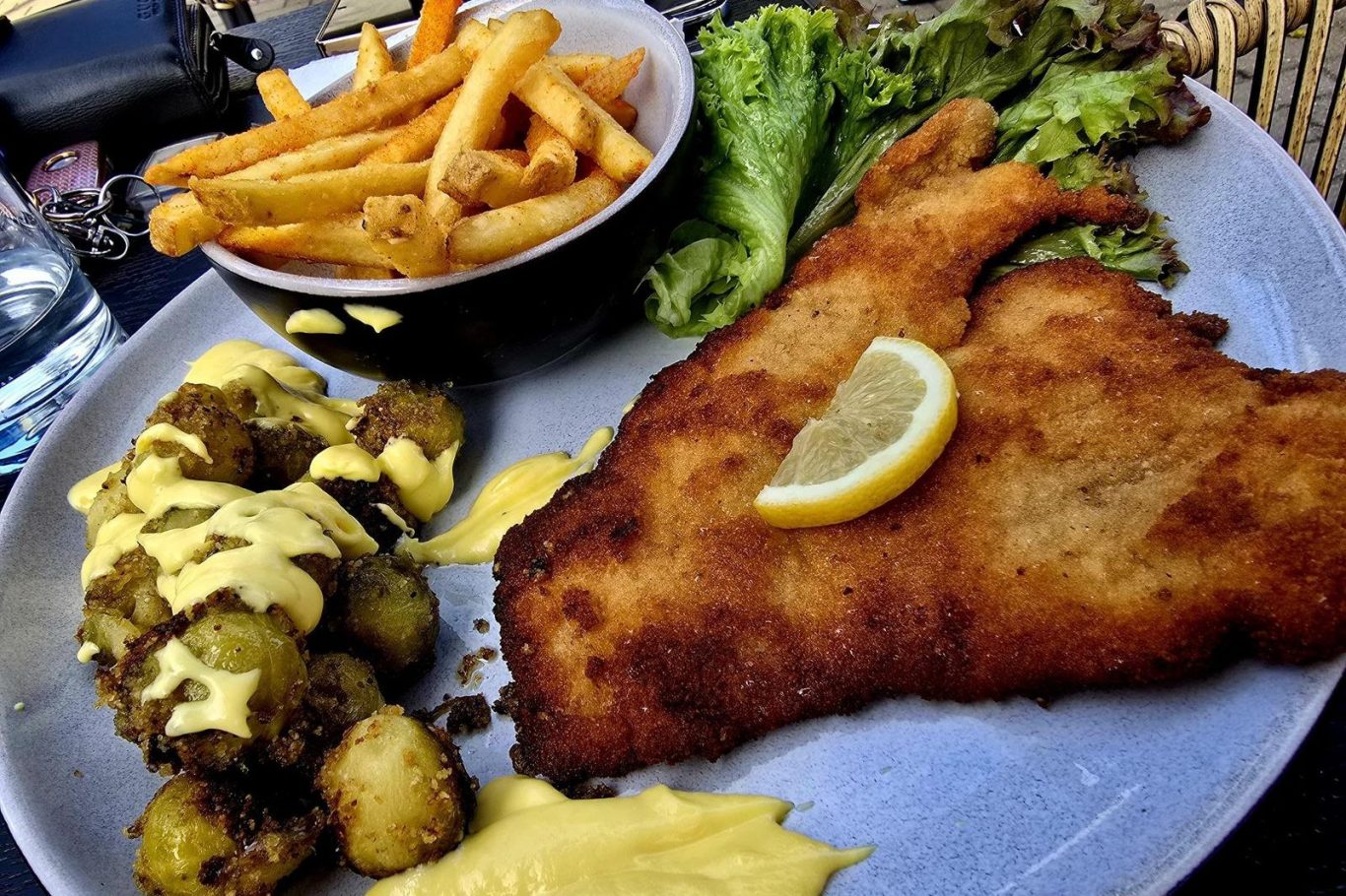 Ein paniertes Fischfilet mit Zitrone, Pommes und Salat auf einem Teller.